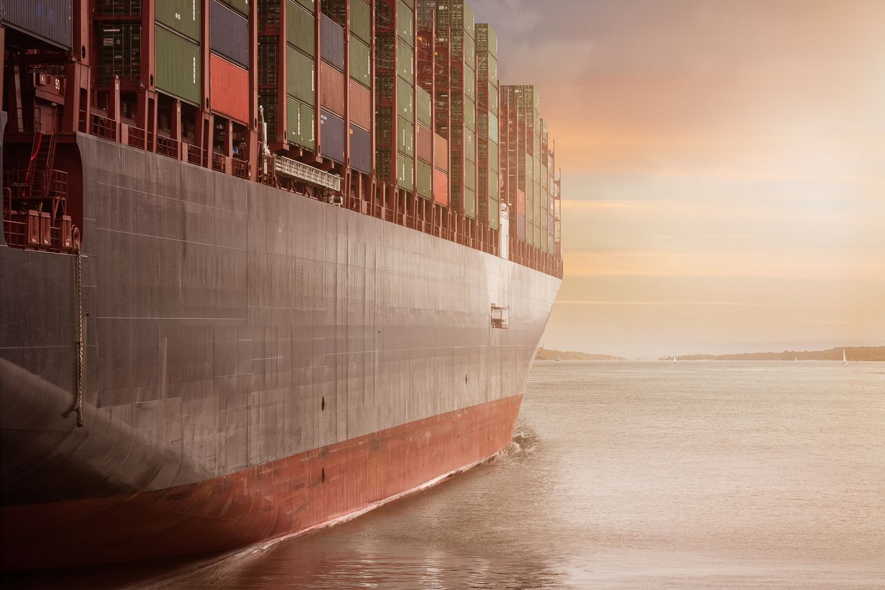 The Art of Drawing Readers In: Your attractive post title goes here A colossal cargo ship loaded with containers navigates through calm waters against a vibrant sunset sky.